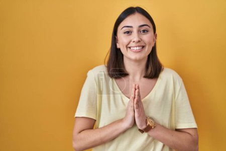 Téléchargez les photos : Hispanic girl wearing casual t shirt over yellow background praying with hands together asking for forgiveness smiling confident. - en image libre de droit