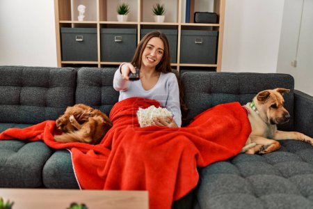 Joven mujer hispana viendo una película sentada en un sofá con perros en casa