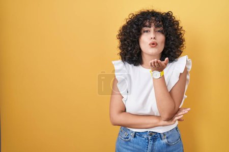 Photo for Young middle east woman standing over yellow background looking at the camera blowing a kiss with hand on air being lovely and sexy. love expression. - Royalty Free Image