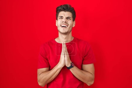 Photo for Young hispanic man standing over red background begging and praying with hands together with hope expression on face very emotional and worried. begging. - Royalty Free Image
