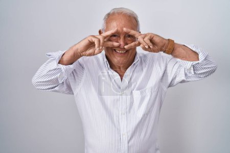 Foto de Senior man with grey hair standing over isolated background doing peace symbol with fingers over face, smiling cheerful showing victory - Imagen libre de derechos