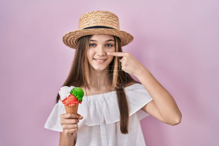 Téléchargez les photos : Teenager girl holding ice cream pointing with hand finger to face and nose, smiling cheerful. beauty concept - en image libre de droit