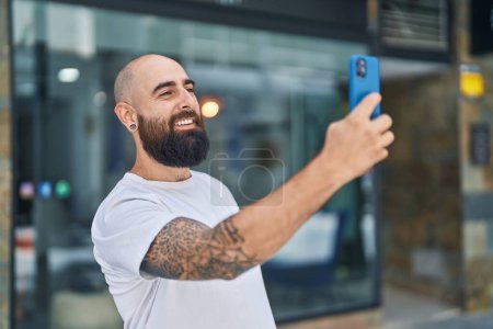 Foto de Joven calvo sonriendo confiado haciendo selfie por el teléfono inteligente en la calle - Imagen libre de derechos