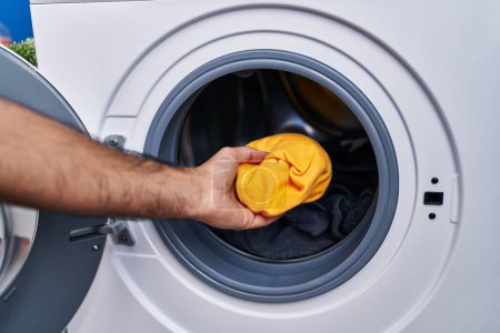 Téléchargez les photos : Jeune homme hispanique mettre des vêtements sur la machine à laver à la buanderie - en image libre de droit