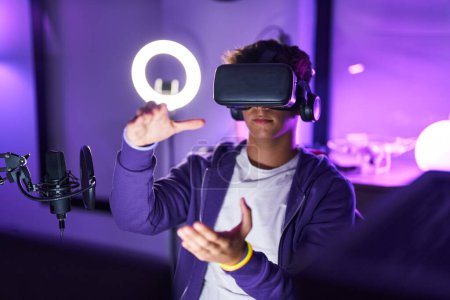 Téléchargez les photos : Young hispanic teenager streamer playing video game using virtual reality glasses at gaming room - en image libre de droit