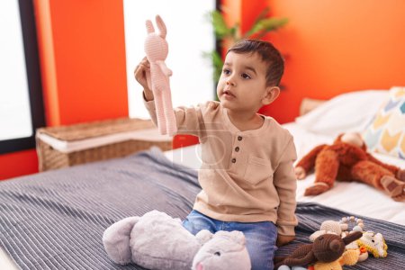 Téléchargez les photos : Adorable bambin hispanique jouant avec des poupées assises sur le lit dans la chambre - en image libre de droit