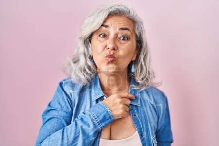 Photo for Middle age woman with grey hair standing over pink background looking at the camera blowing a kiss on air being lovely and sexy. love expression. - Royalty Free Image