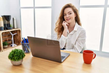 Photo for Young caucasian woman working at the office using computer laptop with hand on chin thinking about question, pensive expression. smiling and thoughtful face. doubt concept. - Royalty Free Image