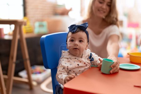 Photo for Woman and toddler learning to eat with plastic dish toy sitting on table at kindergarten - Royalty Free Image