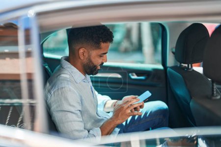 Téléchargez les photos : Jeune homme arabe utilisant smartphone assis sur la voiture à la rue - en image libre de droit