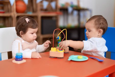Foto de Dos niños pequeños jugando con juguetes sentados en la mesa en el jardín de infantes - Imagen libre de derechos