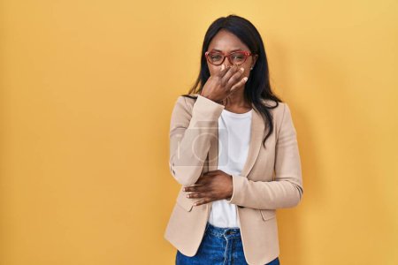 Foto de African young woman wearing glasses smelling something stinky and disgusting, intolerable smell, holding breath with fingers on nose. bad smell - Imagen libre de derechos