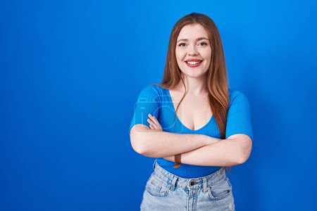 Téléchargez les photos : Redhead woman standing over blue background happy face smiling with crossed arms looking at the camera. positive person. - en image libre de droit