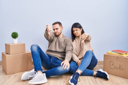 Photo for Young couple moving to a new home looking unhappy and angry showing rejection and negative with thumbs down gesture. bad expression. - Royalty Free Image
