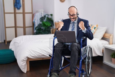 Photo for Hispanic man with beard sitting on wheelchair doing business video call screaming proud, celebrating victory and success very excited with raised arms - Royalty Free Image
