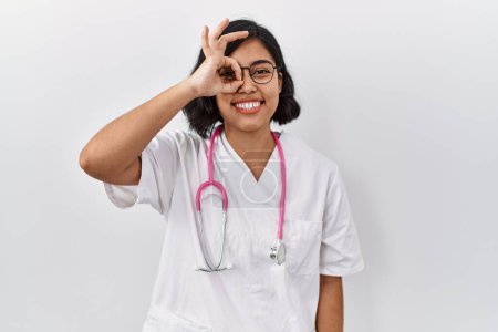 Photo for Young hispanic doctor woman wearing stethoscope over isolated background doing ok gesture with hand smiling, eye looking through fingers with happy face. - Royalty Free Image