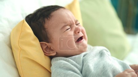Foto de Adorable bebé hispano acostado en la cama llorando en el dormitorio - Imagen libre de derechos
