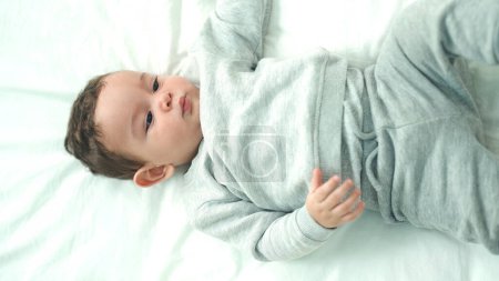 Photo for Adorable hispanic baby lying on bed with relaxed expression at bedroom - Royalty Free Image