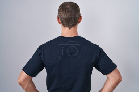 Téléchargez les photos : Blanc blond homme portant Bitcoin t-shirt debout vers l'arrière regardant loin avec les bras sur le corps - en image libre de droit