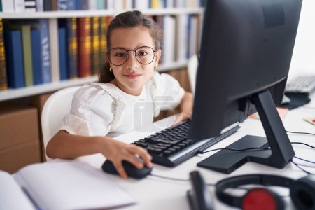 Téléchargez les photos : Adorable étudiante hispanique utilisant l'ordinateur assis sur la table en classe - en image libre de droit