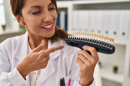 Téléchargez les photos : Jeune femme latine portant un uniforme de dentiste tenant un test de blanchiment à la clinique - en image libre de droit