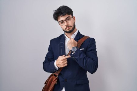 Photo for Hispanic man with beard wearing business clothes in hurry pointing to watch time, impatience, looking at the camera with relaxed expression - Royalty Free Image