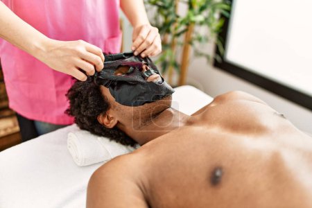 Téléchargez les photos : Jeune homme afro-américain ayant traitement du visage de la peau au centre de beauté - en image libre de droit