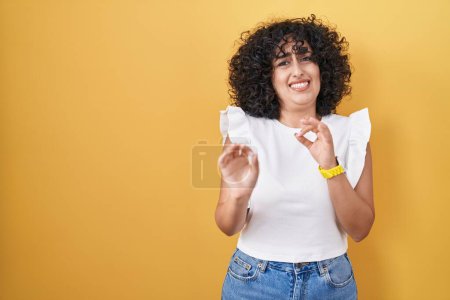 Foto de Young middle east woman standing over yellow background disgusted expression, displeased and fearful doing disgust face because aversion reaction. with hands raised - Imagen libre de derechos