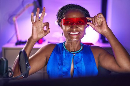 Téléchargez les photos : African woman with dreadlocks playing video games wearing virtual reality glasses doing ok sign with fingers, smiling friendly gesturing excellent symbol - en image libre de droit