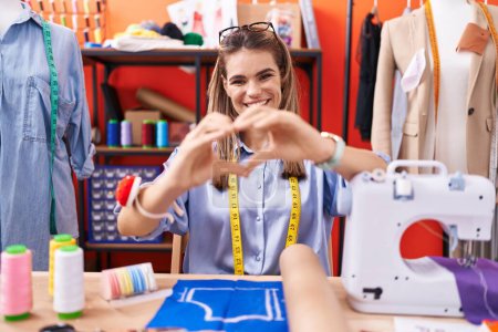 Photo for Hispanic young woman dressmaker designer at atelier room smiling in love doing heart symbol shape with hands. romantic concept. - Royalty Free Image