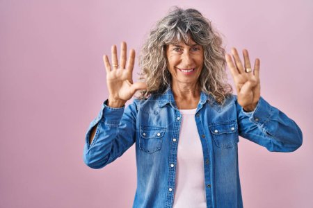 Téléchargez les photos : Middle age woman standing over pink background showing and pointing up with fingers number nine while smiling confident and happy. - en image libre de droit
