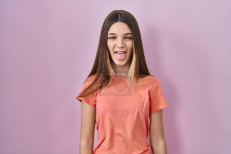 Foto de Teenager girl standing over pink background sticking tongue out happy with funny expression. emotion concept. - Imagen libre de derechos