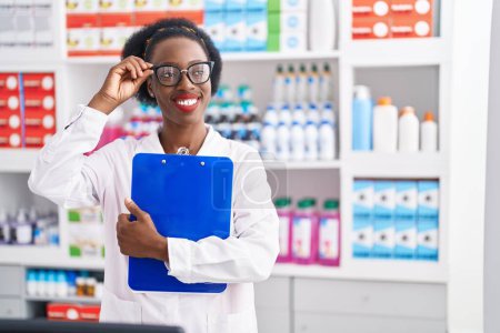 Photo for African american woman pharmacist smiling confident holding clipboard at pharmacy - Royalty Free Image