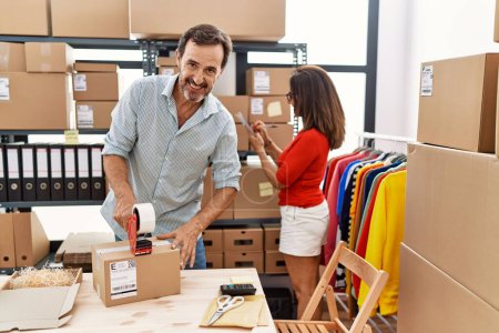 Middle age man and woman business partners smiling confident packing package at storehouse