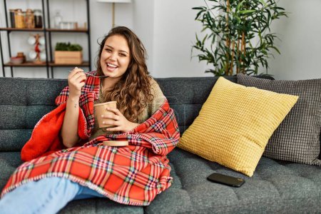 Photo for Young beautiful hispanic woman eating ice cream sitting on sofa at home - Royalty Free Image