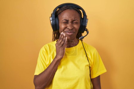Foto de African american woman listening to music using headphones touching mouth with hand with painful expression because of toothache or dental illness on teeth. dentist - Imagen libre de derechos