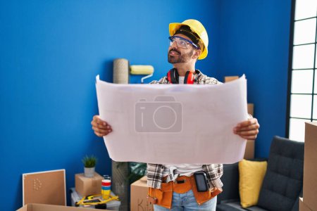 Foto de Joven trabajador hispano sonriendo confiado mirando planos en nuevo hogar - Imagen libre de derechos