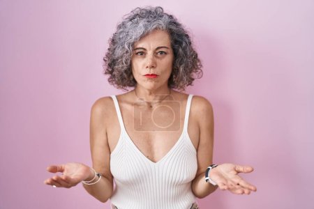 Photo for Middle age woman with grey hair standing over pink background clueless and confused with open arms, no idea concept. - Royalty Free Image