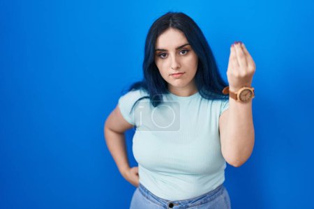 Foto de Joven chica moderna con el pelo azul de pie sobre fondo azul haciendo gesto italiano con la mano y los dedos expresión de confianza - Imagen libre de derechos