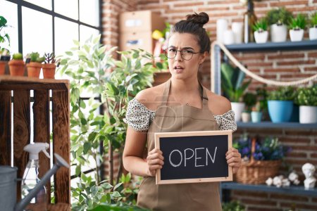 Photo for Hispanic woman working at florist holding open sign clueless and confused expression. doubt concept. - Royalty Free Image
