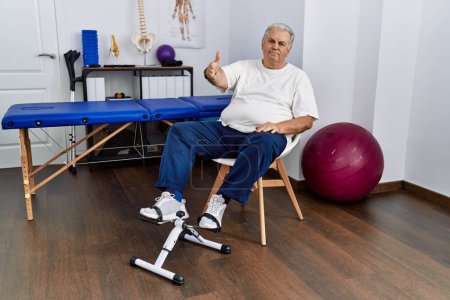 Photo for Senior caucasian man at physiotherapy clinic using pedal exerciser smiling friendly offering handshake as greeting and welcoming. successful business. - Royalty Free Image