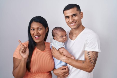 Photo for Young hispanic couple with baby standing together over isolated background with a big smile on face, pointing with hand finger to the side looking at the camera. - Royalty Free Image