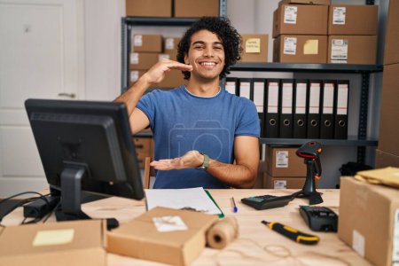 Foto de Hispanic man with curly hair working at small business ecommerce gesturing with hands showing big and large size sign, measure symbol. smiling looking at the camera. measuring concept. - Imagen libre de derechos