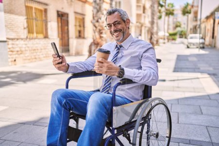 Foto de Hombre hispano de mediana edad sentado en silla de ruedas usando smartphone en la calle - Imagen libre de derechos