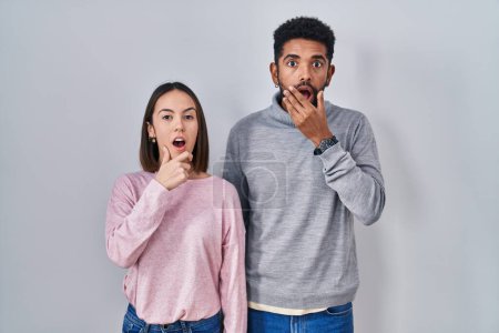 Photo for Young hispanic couple standing together looking fascinated with disbelief, surprise and amazed expression with hands on chin - Royalty Free Image