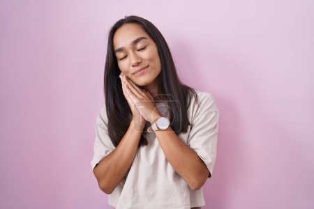 Photo for Young hispanic woman standing over pink background sleeping tired dreaming and posing with hands together while smiling with closed eyes. - Royalty Free Image