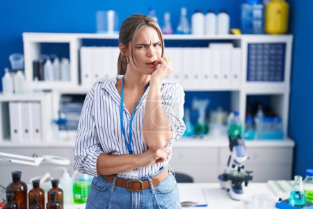 Photo for Young beautiful woman working at scientist laboratory looking stressed and nervous with hands on mouth biting nails. anxiety problem. - Royalty Free Image