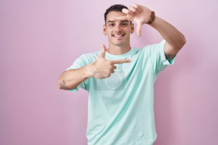 Téléchargez les photos : Bel homme hispanique debout sur fond rose souriant faisant cadre avec les mains et les doigts avec le visage heureux. concept de créativité et photographie. - en image libre de droit