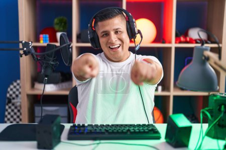 Photo for Young hispanic man playing video games pointing to you and the camera with fingers, smiling positive and cheerful - Royalty Free Image