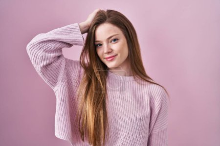 Foto de Joven mujer caucásica de pie sobre fondo rosa sonriendo seguro de tocar el cabello con la mano hacia arriba gesto, posando atractivo y de moda - Imagen libre de derechos